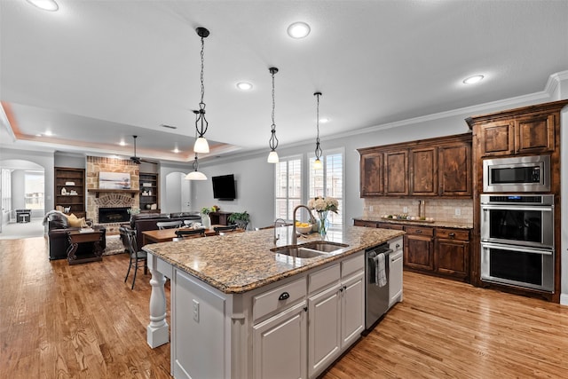 kitchen with arched walkways, a kitchen island with sink, a fireplace, a sink, and appliances with stainless steel finishes