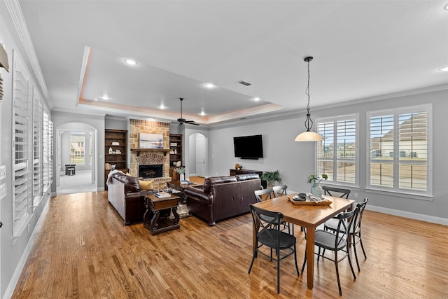 dining area featuring arched walkways, a tray ceiling, a fireplace, and visible vents