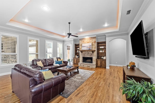 living room featuring arched walkways, visible vents, light wood-style floors, a tray ceiling, and crown molding