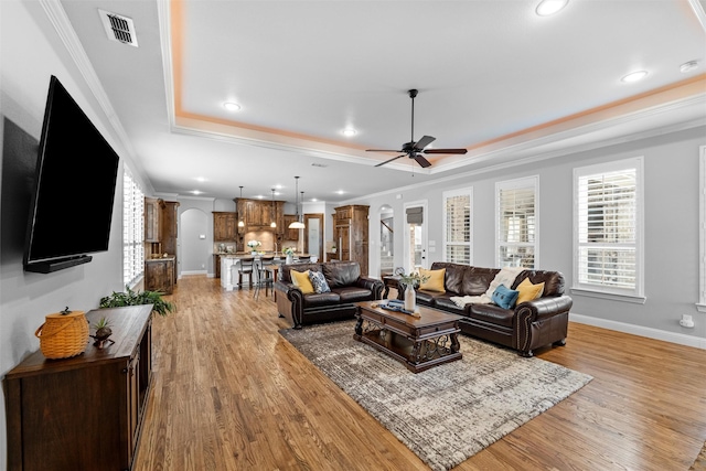 living room featuring arched walkways, visible vents, plenty of natural light, and a tray ceiling