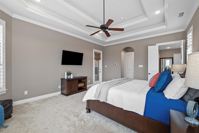 carpeted bedroom featuring a tray ceiling, arched walkways, crown molding, visible vents, and baseboards