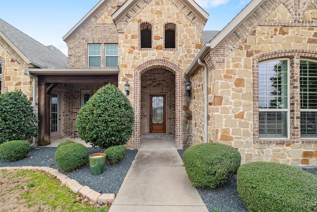 doorway to property featuring stone siding, brick siding, and roof with shingles