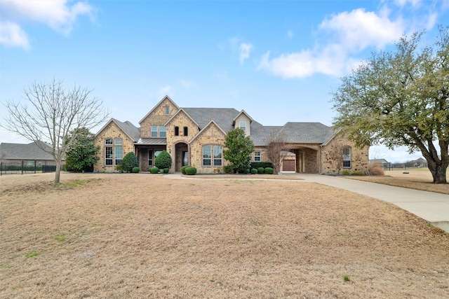 french provincial home featuring metal roof, fence, driveway, stone siding, and a standing seam roof