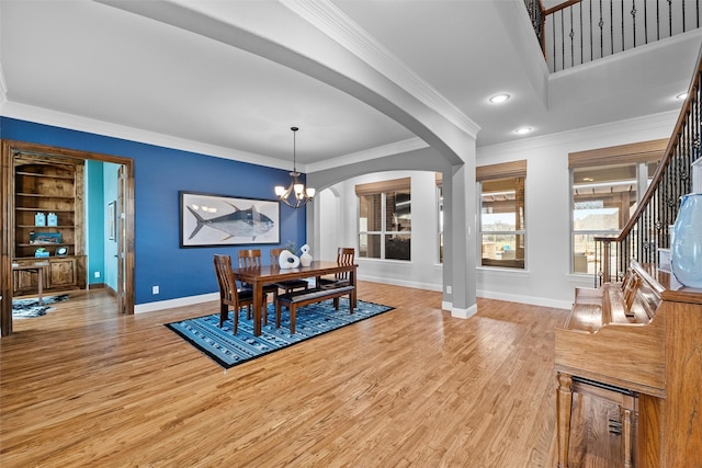 dining space with light wood finished floors, baseboards, arched walkways, ornamental molding, and a notable chandelier