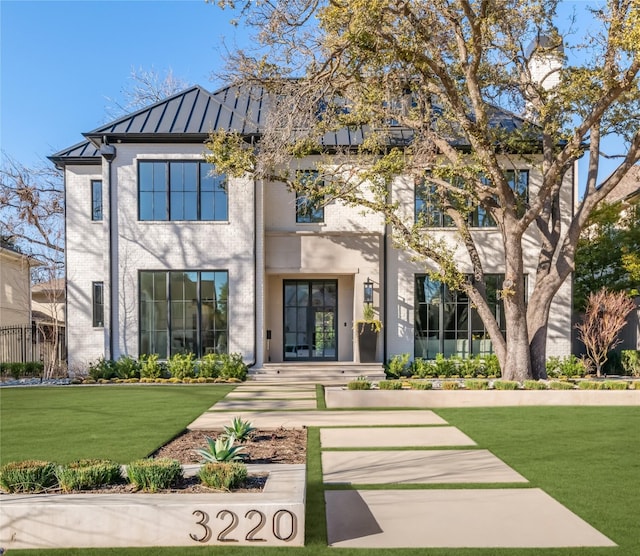 view of front of property featuring metal roof, brick siding, a standing seam roof, and a front lawn