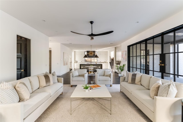 living area featuring light wood-type flooring, ceiling fan, baseboards, and stairs