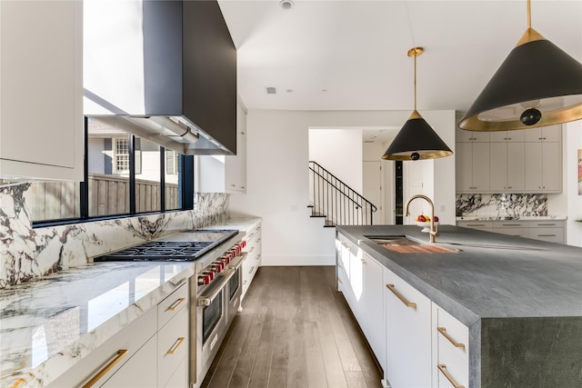 kitchen with range with two ovens, range hood, dark wood finished floors, decorative backsplash, and a sink