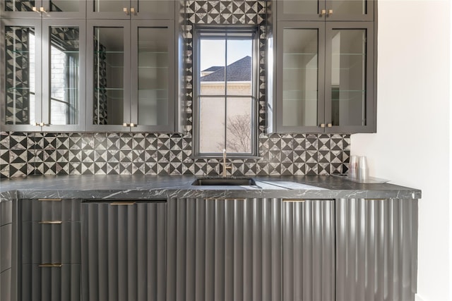 kitchen featuring dark countertops, glass insert cabinets, gray cabinets, and a sink