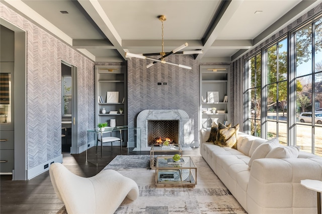 living room with built in features, a large fireplace, wood finished floors, beamed ceiling, and wallpapered walls