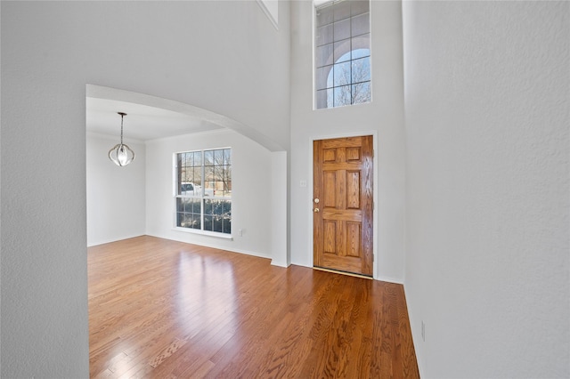 foyer entrance featuring arched walkways, crown molding, a towering ceiling, wood finished floors, and baseboards