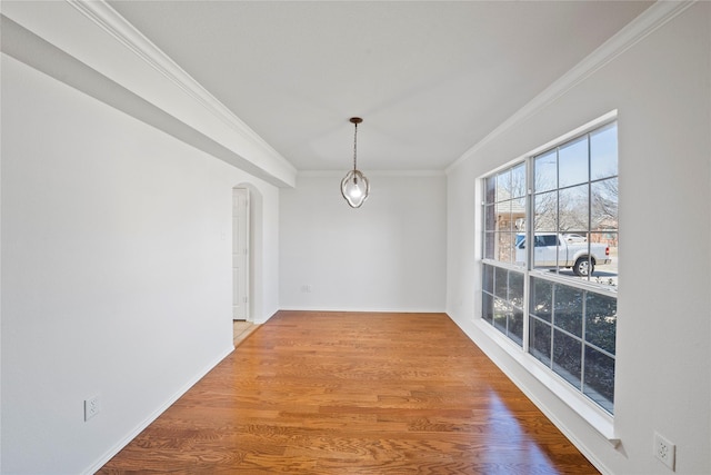unfurnished dining area featuring ornamental molding, arched walkways, wood finished floors, and baseboards
