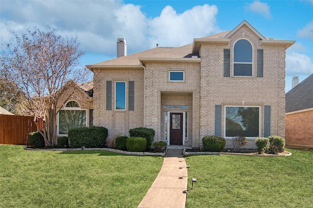 traditional-style home with brick siding, a front lawn, a chimney, and fence