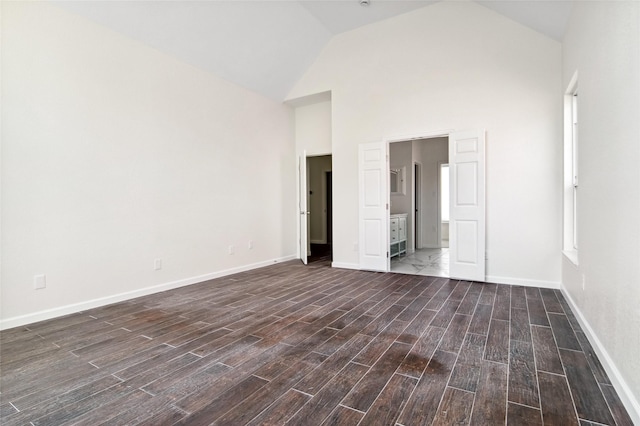 unfurnished bedroom with high vaulted ceiling, ensuite bath, baseboards, and dark wood-style flooring