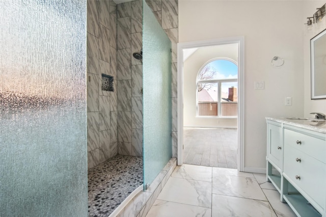 bathroom featuring marble finish floor, a tile shower, vanity, and baseboards