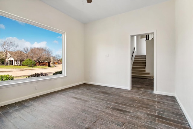 empty room featuring a ceiling fan, dark wood-style flooring, stairway, and baseboards