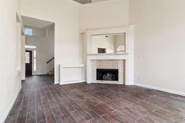 unfurnished living room with baseboards, a tiled fireplace, stairway, wood finished floors, and a high ceiling