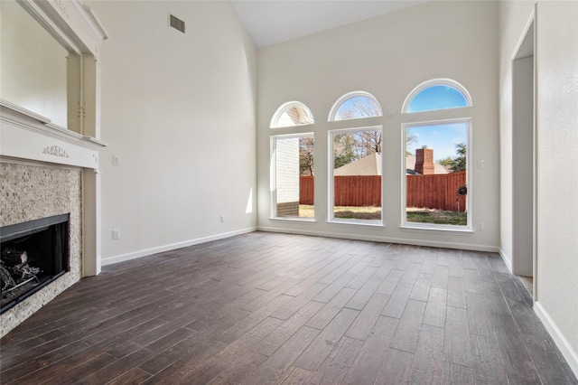 unfurnished living room with dark wood-type flooring, a high ceiling, visible vents, baseboards, and a tiled fireplace