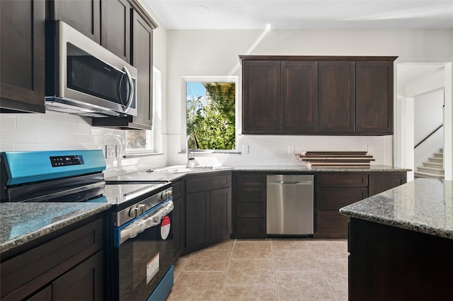 kitchen with decorative backsplash, appliances with stainless steel finishes, dark brown cabinetry, a sink, and light stone countertops