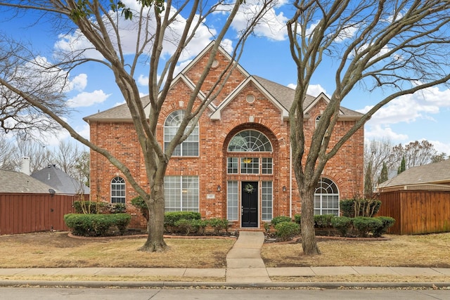 traditional-style house with a front yard, brick siding, fence, and roof with shingles