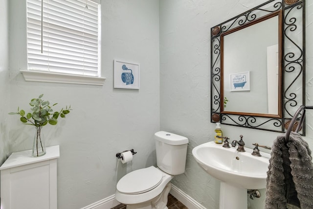 half bathroom with toilet, baseboards, and a sink