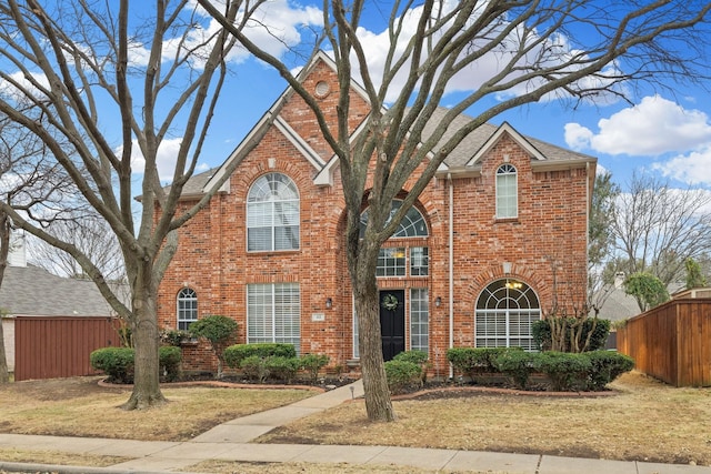 traditional home featuring a shingled roof, brick siding, fence, and a front lawn