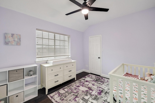 bedroom featuring lofted ceiling, a ceiling fan, baseboards, dark wood-style floors, and a crib