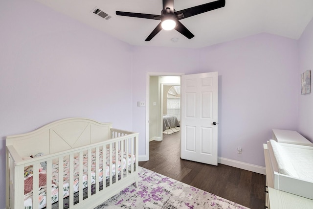 bedroom with lofted ceiling, visible vents, wood finished floors, a nursery area, and baseboards