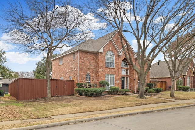 view of front facade with a front yard, brick siding, fence, and roof with shingles