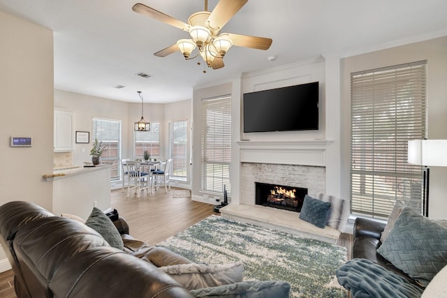 living room featuring visible vents, ornamental molding, wood finished floors, and a stone fireplace