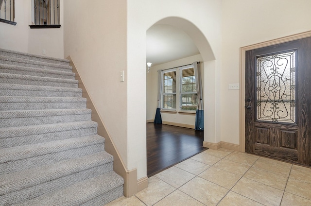 foyer with baseboards, stairway, arched walkways, a towering ceiling, and light tile patterned flooring