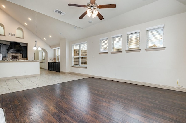 unfurnished living room with ceiling fan, visible vents, arched walkways, and light wood-style flooring