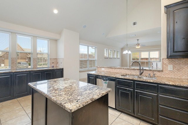 kitchen with a sink, stainless steel dishwasher, a center island, lofted ceiling, and light stone countertops