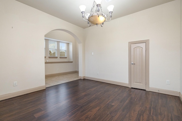 empty room with a notable chandelier, wood finished floors, arched walkways, and baseboards