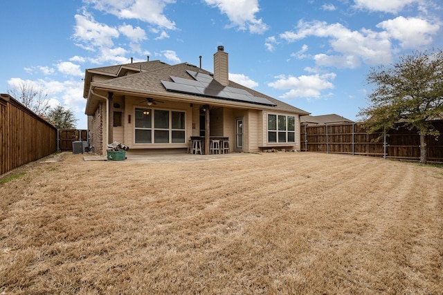 rear view of property featuring a ceiling fan, roof mounted solar panels, a patio, a fenced backyard, and a chimney