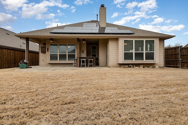 back of property with a ceiling fan, roof mounted solar panels, a fenced backyard, a yard, and a patio area