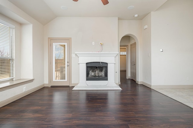 unfurnished living room featuring ceiling fan, a fireplace with raised hearth, a healthy amount of sunlight, and wood finished floors