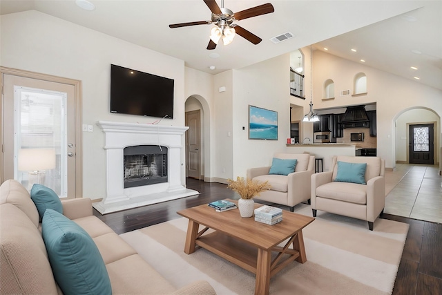 living area with wood finished floors, visible vents, high vaulted ceiling, a fireplace with raised hearth, and arched walkways