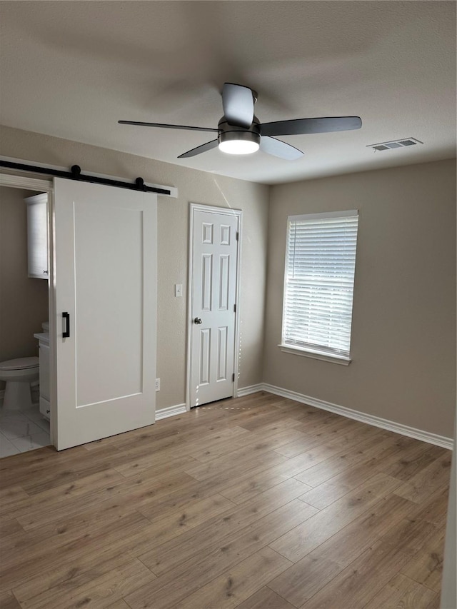 unfurnished bedroom featuring ensuite bath, a barn door, visible vents, and wood finished floors