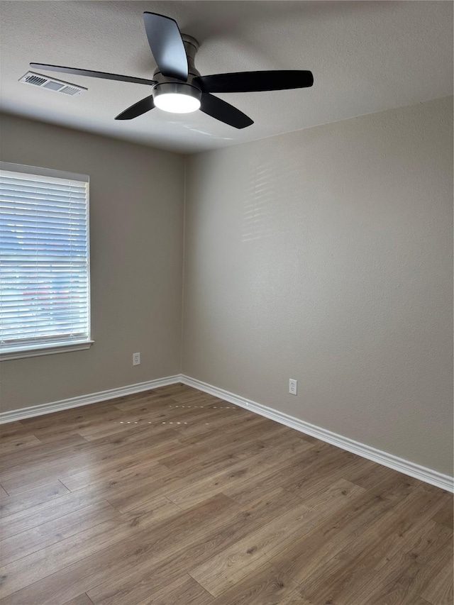 spare room with wood finished floors, visible vents, and baseboards