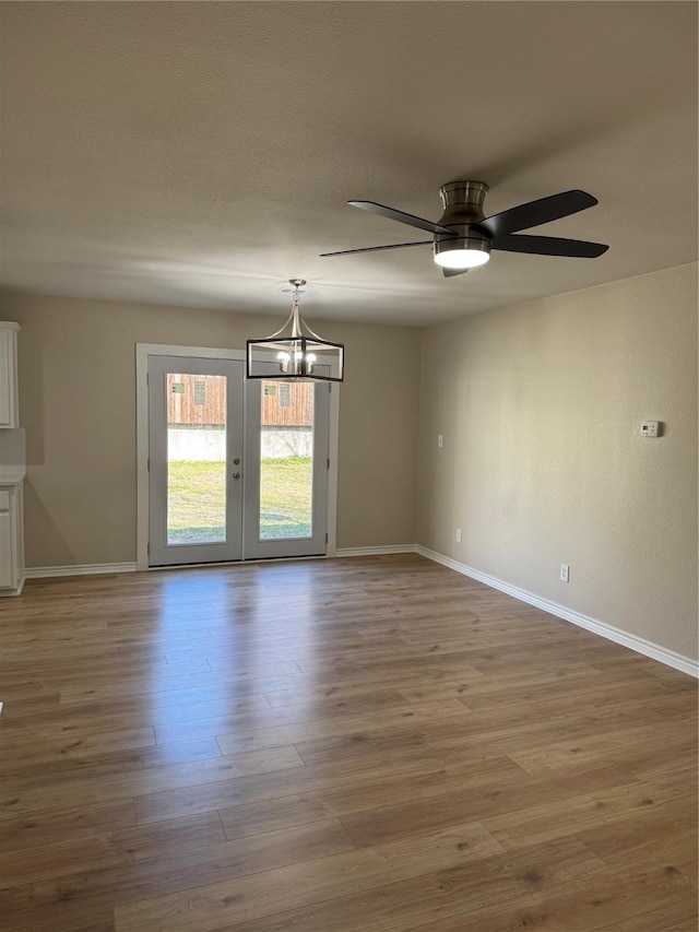 unfurnished room featuring ceiling fan with notable chandelier, wood finished floors, and baseboards