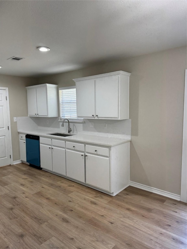 kitchen with light wood-style flooring, white cabinets, a sink, dishwasher, and baseboards