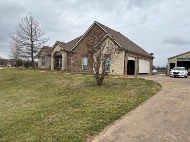 view of front of home with an attached garage, driveway, a front yard, and brick siding