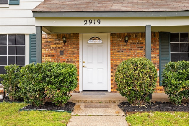 entrance to property with covered porch, brick siding, and roof with shingles