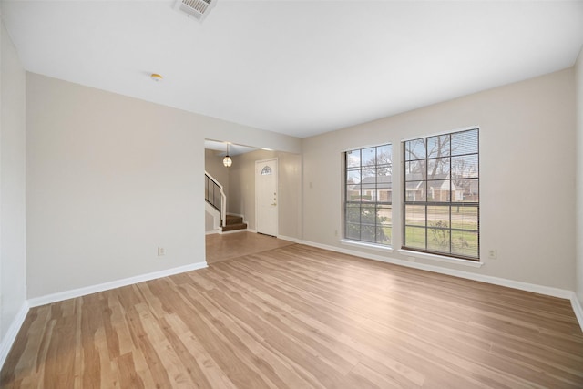 empty room with stairs, baseboards, visible vents, and light wood-style floors