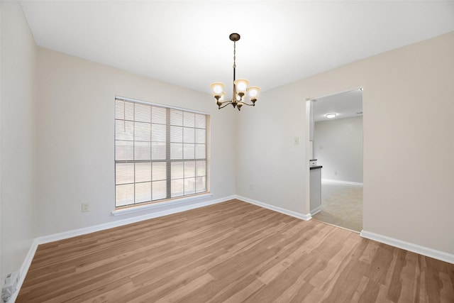 spare room with light wood-type flooring, baseboards, and a chandelier