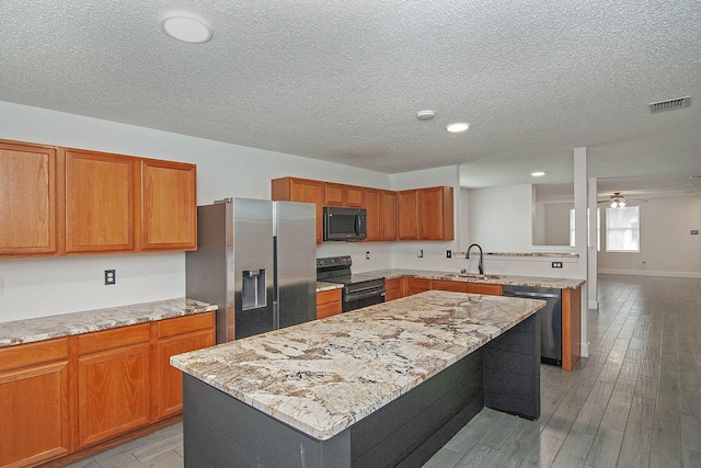 kitchen featuring visible vents, a kitchen island, a sink, light stone countertops, and black appliances