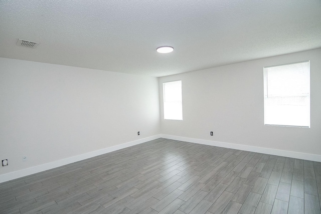 spare room with a textured ceiling, dark wood finished floors, visible vents, and baseboards