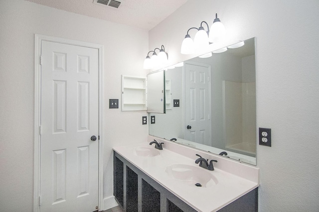 full bath featuring a textured ceiling, double vanity, a sink, and visible vents