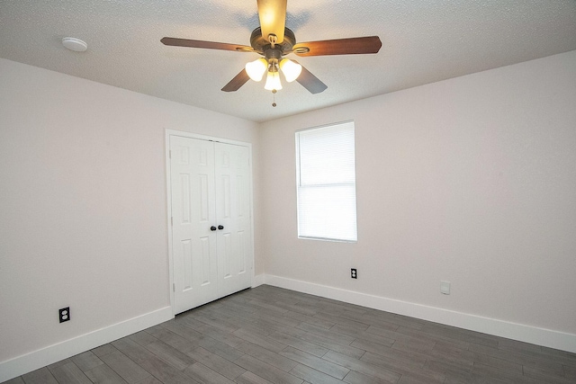 unfurnished bedroom featuring a textured ceiling, dark wood-type flooring, a closet, and baseboards