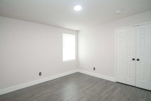 unfurnished bedroom with a closet, dark wood-style flooring, a textured ceiling, and baseboards